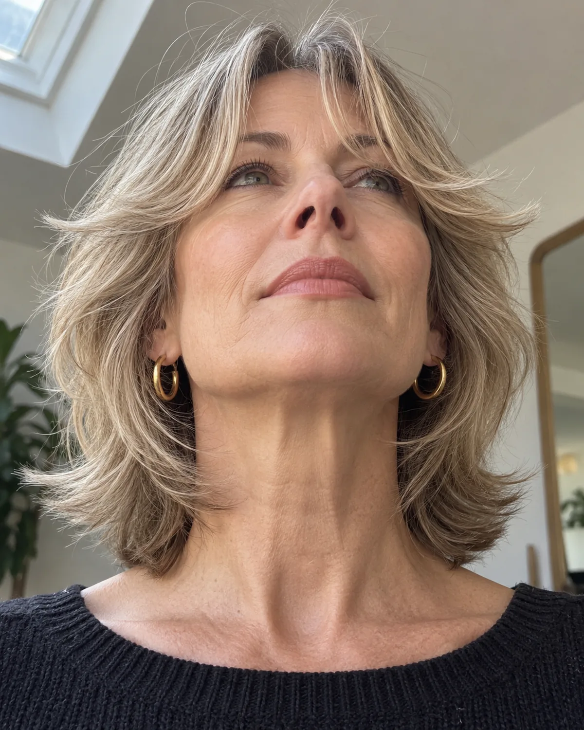 Low-angle view looking up at mature woman with fine hair showing layered bangs curving outward at the tips, creating width and movement