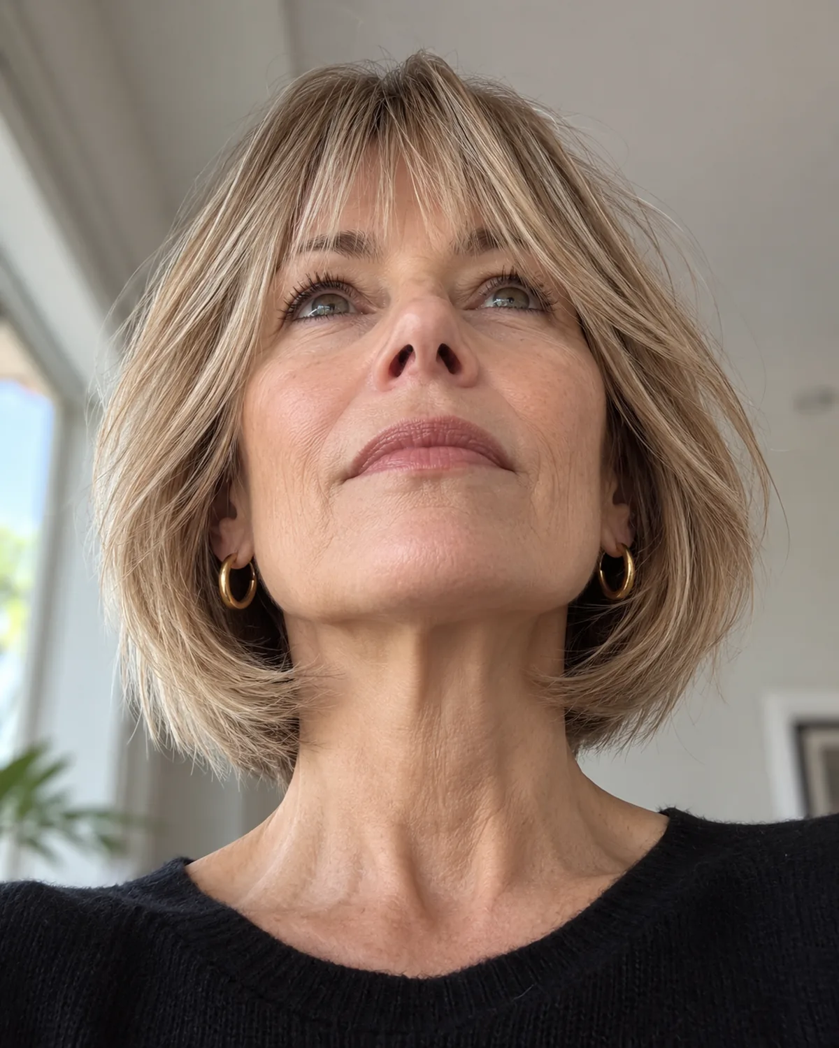 Low-angle view looking up at mature woman's fringe showing a soft A-line shape, shorter at the centre and gradually longer toward the temples, blending into side hair