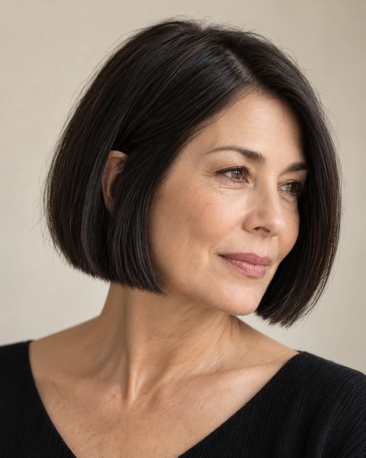 Three-quarter view of woman over 50 with dark blunt bob at jaw length, clean hemline visible against skin