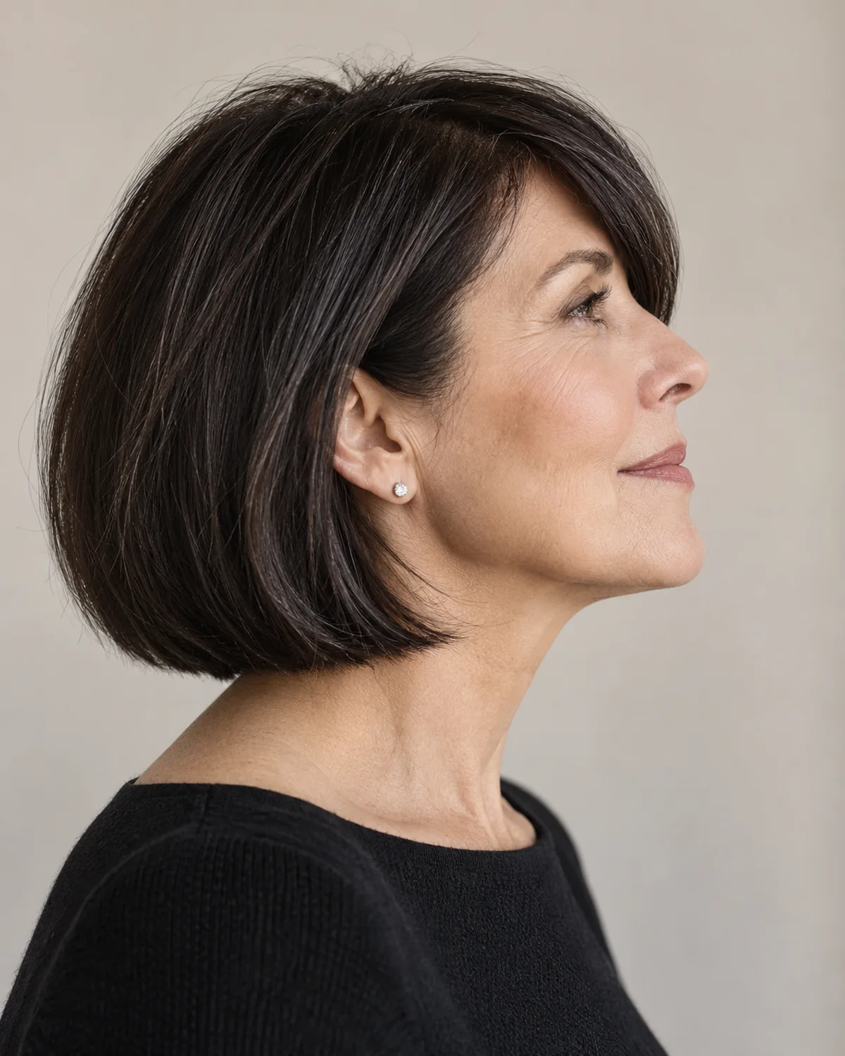 Full profile of woman over 50 with dark chin-length bob and side-swept fringe, bob silhouette and fringe line visible from the side