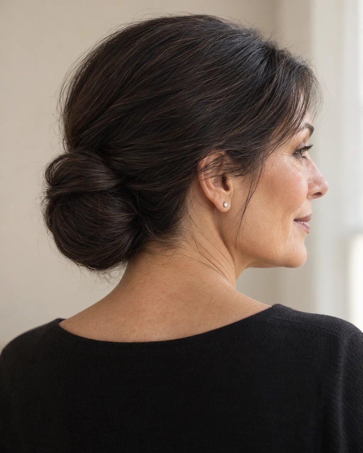 Back three-quarter view of woman over 50 with dark hair gathered in a low chignon at the nape, blunt ends forming a clean knot shape