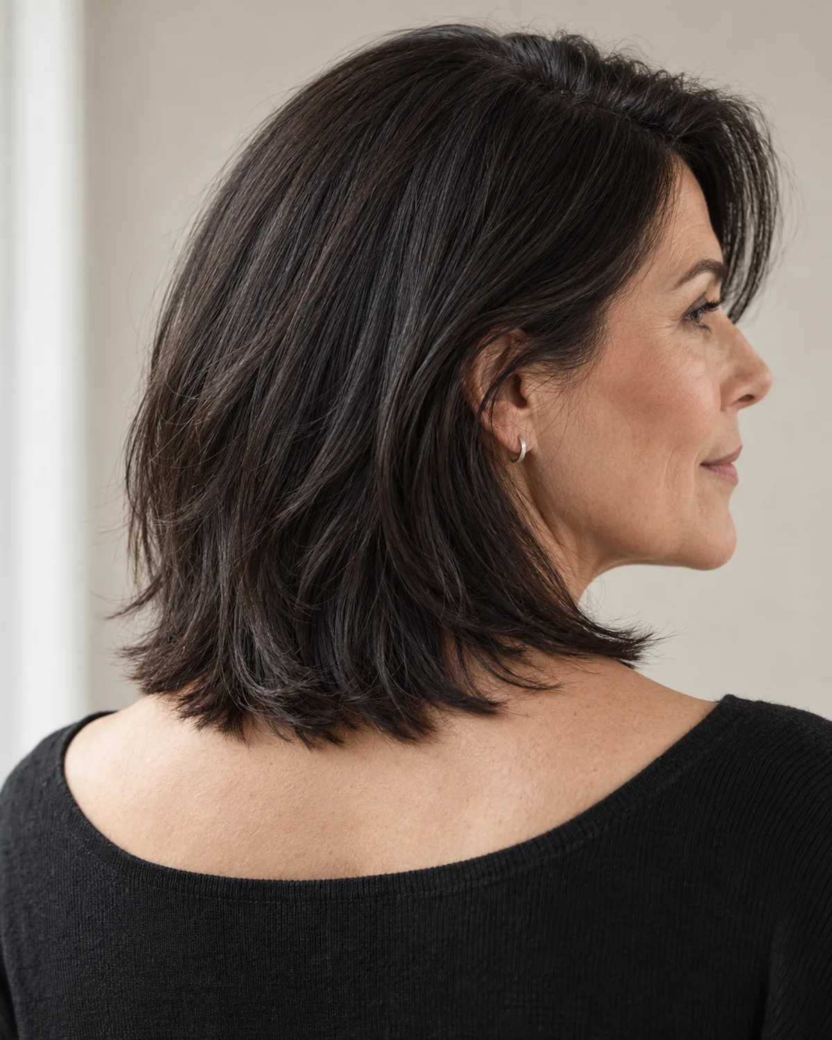 Back three-quarter view of woman over 50 with dark collarbone-length hair showing solid perimeter edge with interior movement