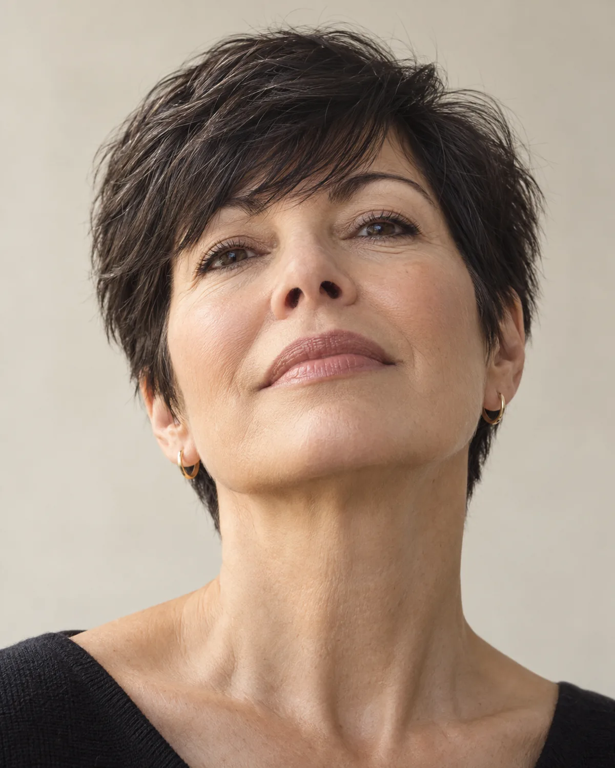 Front view of woman over 50 with dark short crop directed forward over the forehead, chin slightly lifted, textured pieces covering the front hairline