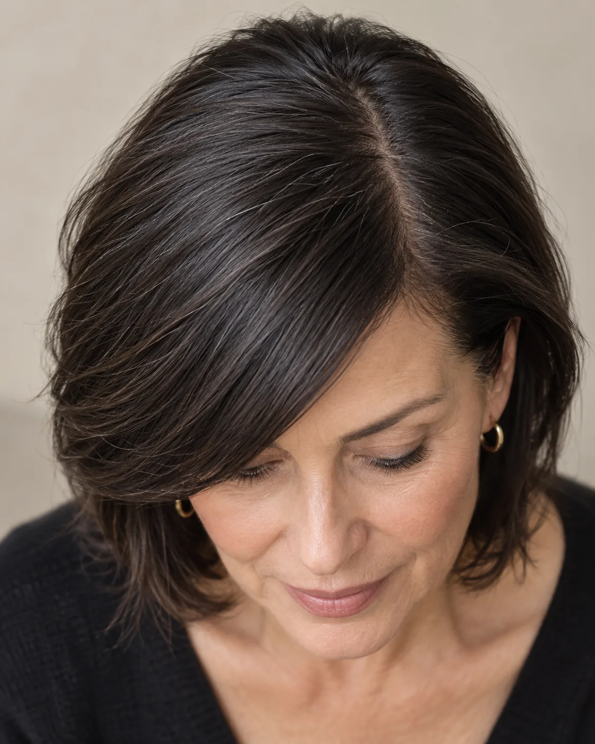 Overhead view of woman over 50 with dark hair and long side-swept bangs across the forehead, swept from a deep side part