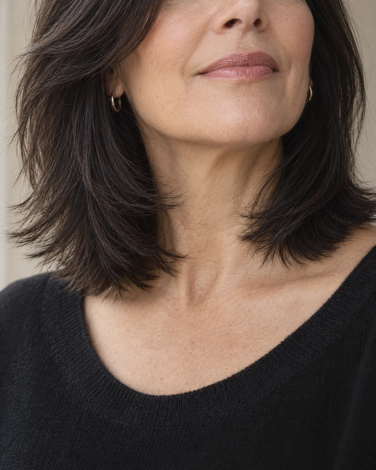 Close crop from chin to shoulder showing woman over 50 with dark shoulder-length hair, razored feathered ends visible at the hemline