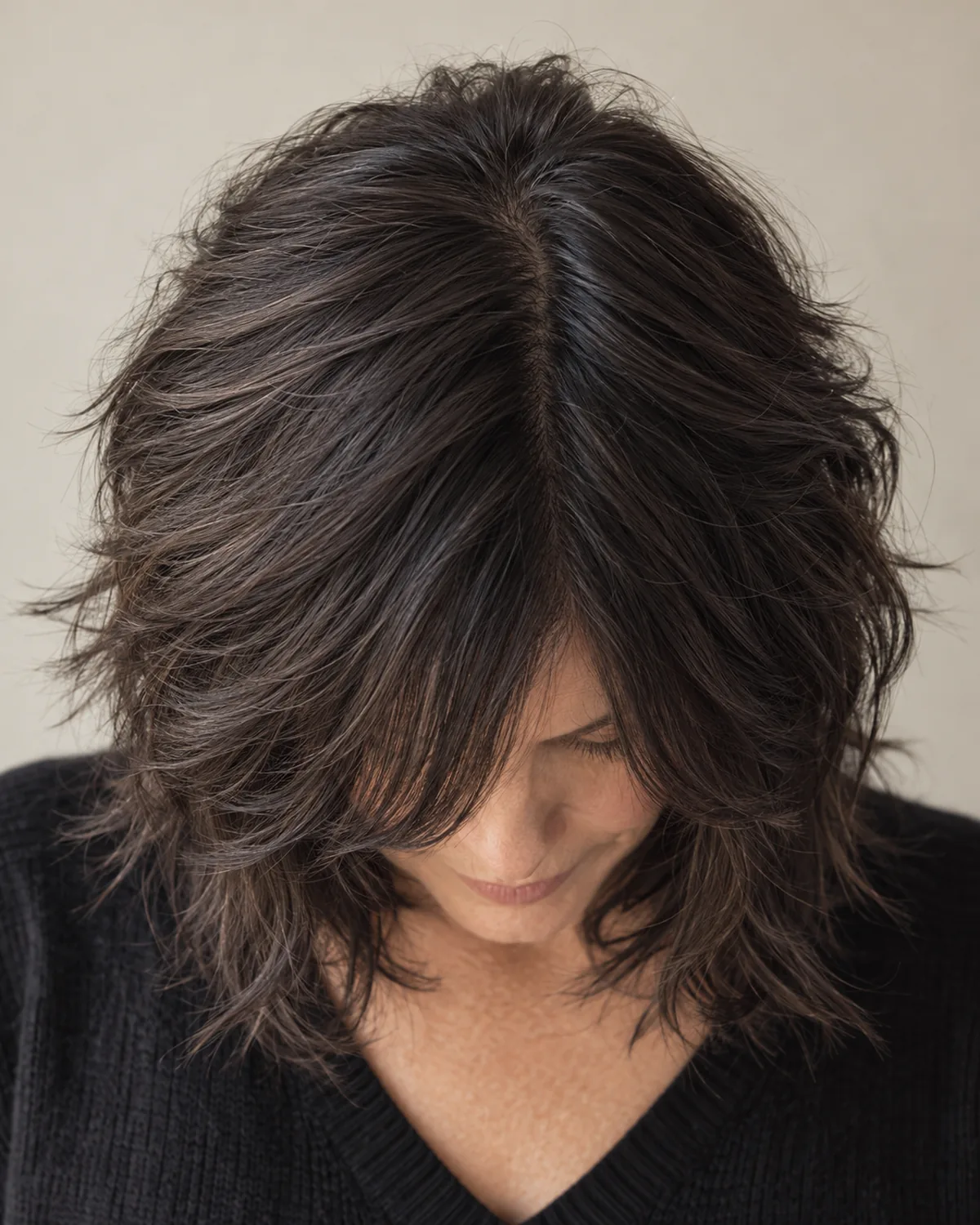 Woman over 50 tilting head forward showing dark shag cut with layered texture throughout the crown and face-framing wisps