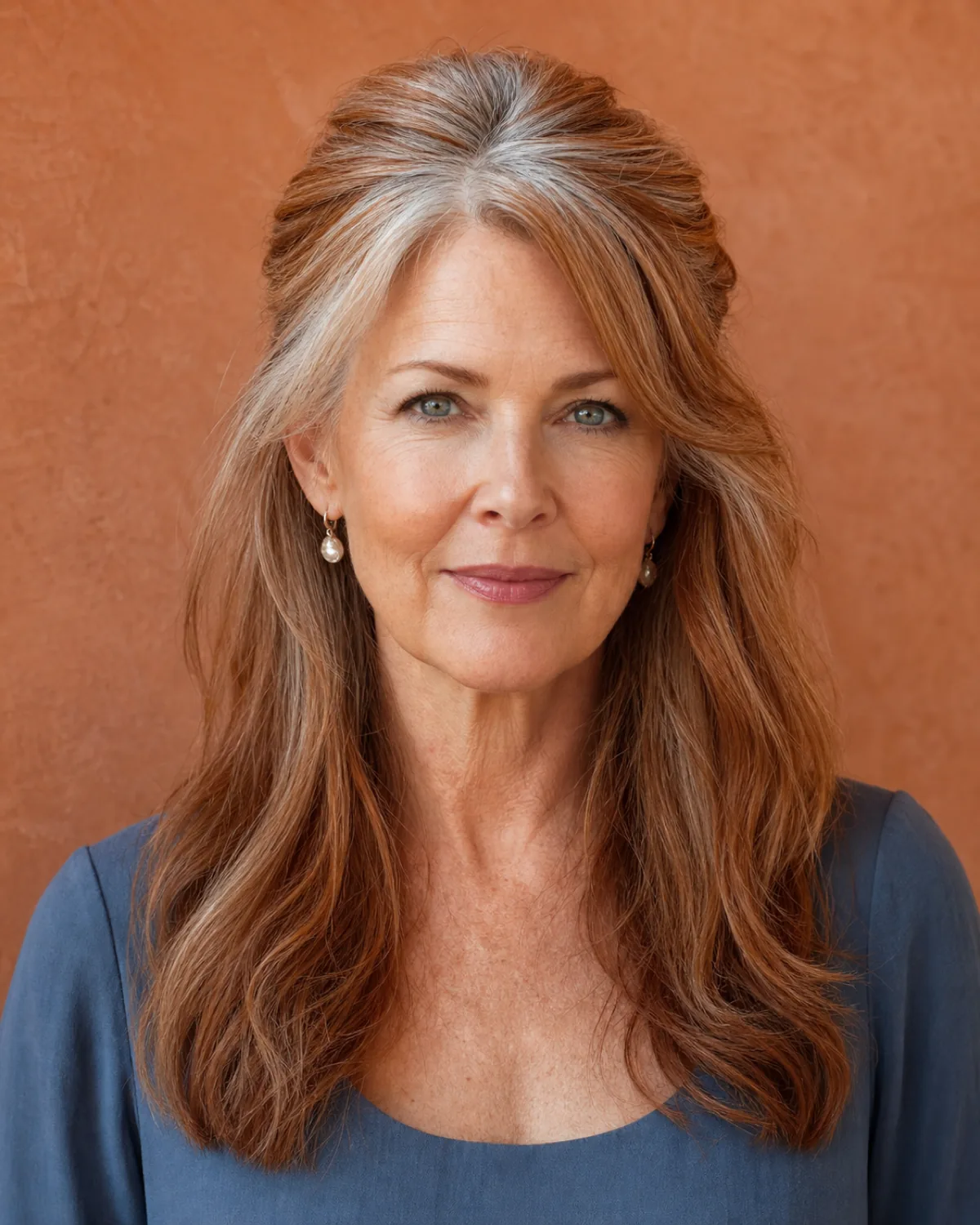 A woman in her late 50s facing the camera with warm brown hair, the top section pinned at the crown with visible lift, the lower half falling in loose waves past her shoulders, soft light from camera left