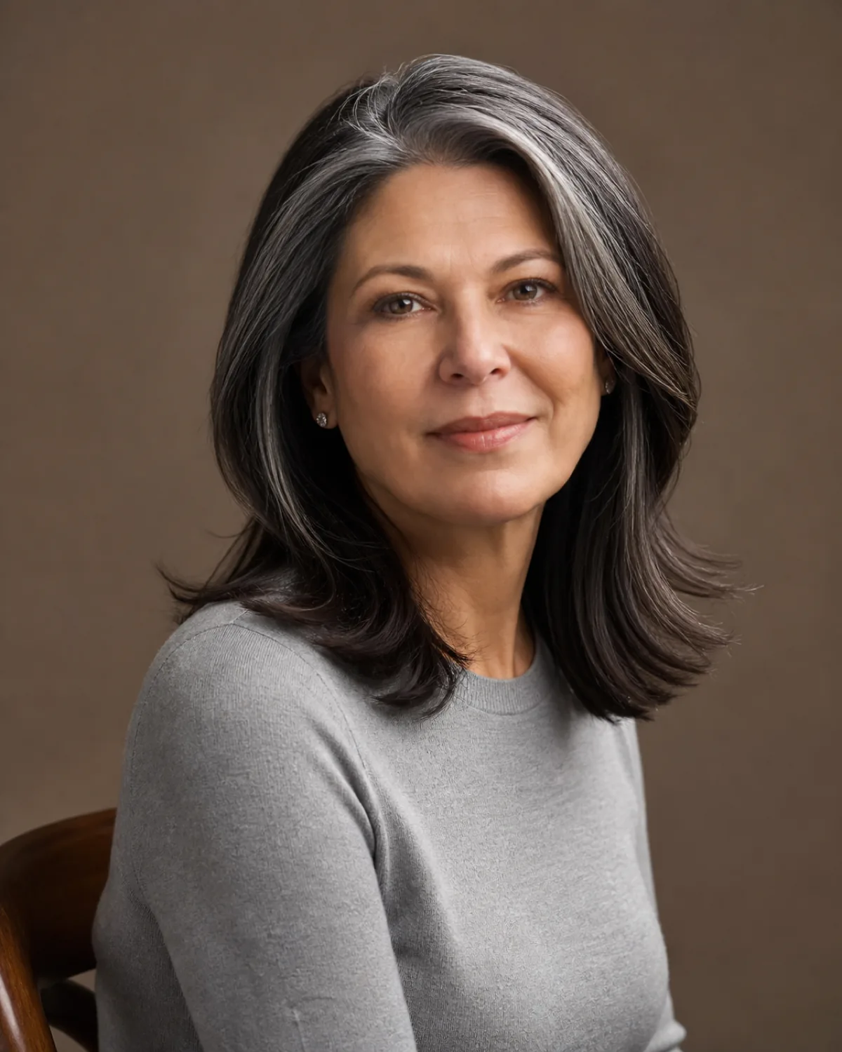 A woman in her late 50s with medium-brown hair in a chin-length layered cut, seated and turned slightly to the side, the hair framing the jawline with visible layers
