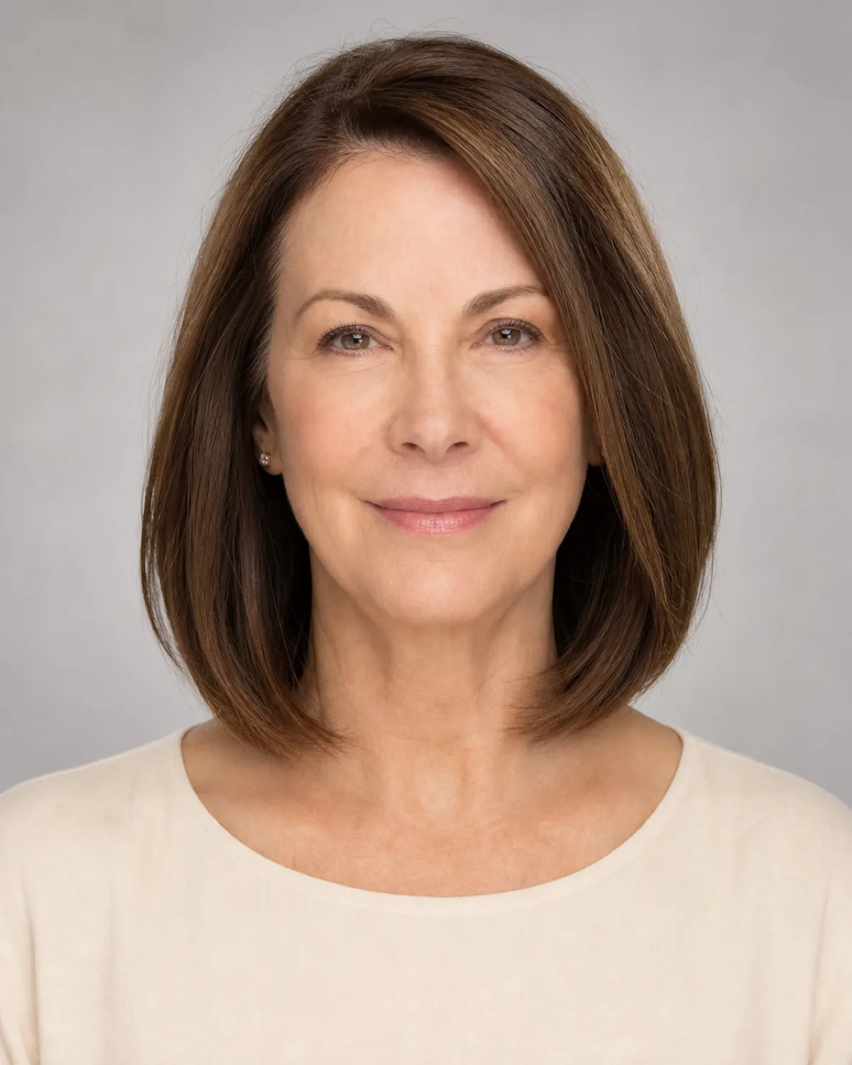 A woman in her early 60s with warm brown hair in a long bob ending between the chin and collarbone, front-facing with the lob adding visual weight in the lower third of her face