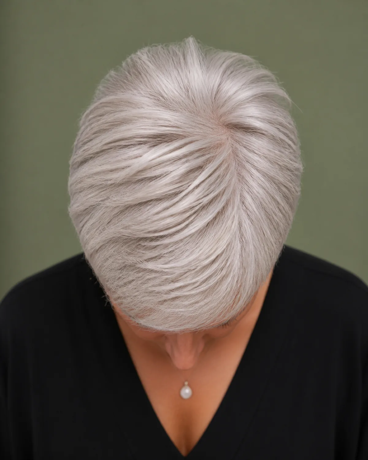 Top-down view showing a silver-white pixie cut with visible crown volume standing taller than the close-cropped sides, sage green background