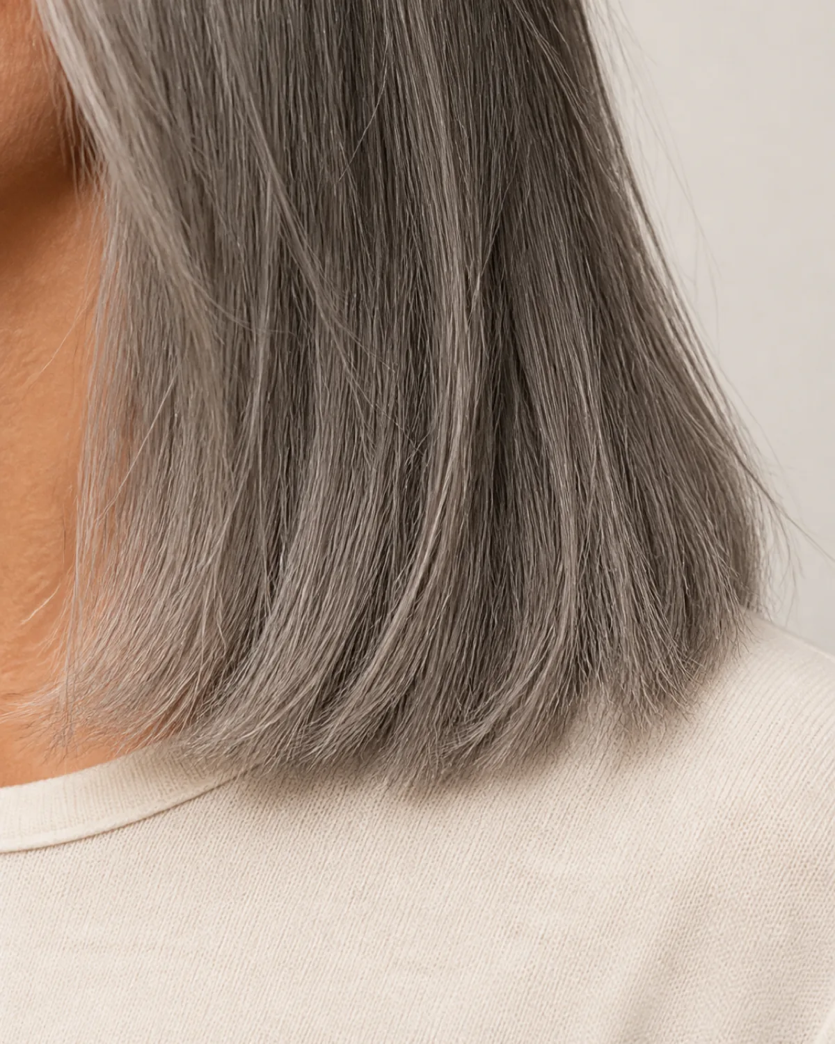 Close crop on grey hair ends at shoulder level showing individually resolved strands, the density at the tips visible against a cream knit top