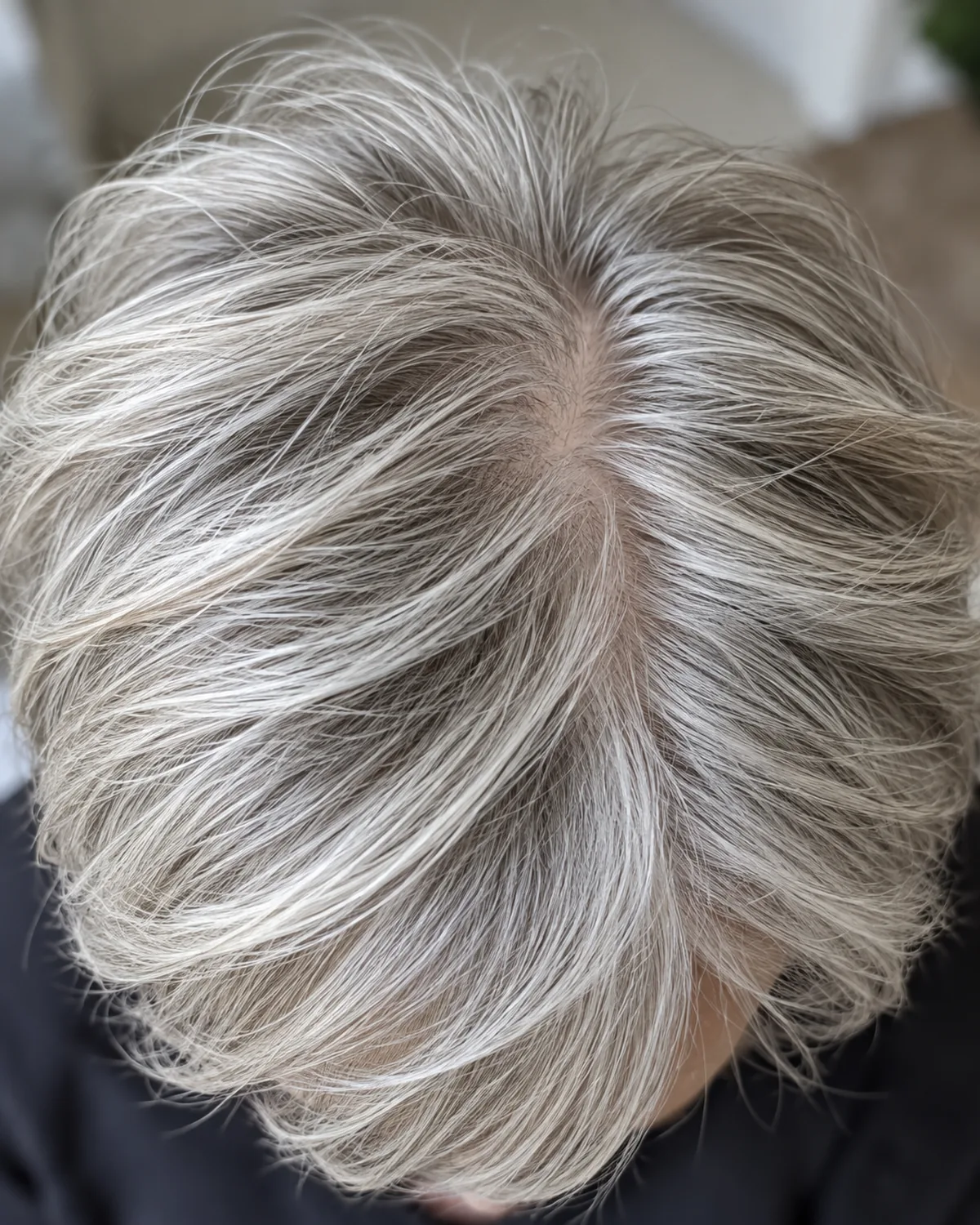 Top-down view of mature woman with fine straight silver hair in a soft-layered pixie, crown layers creating visible root lift