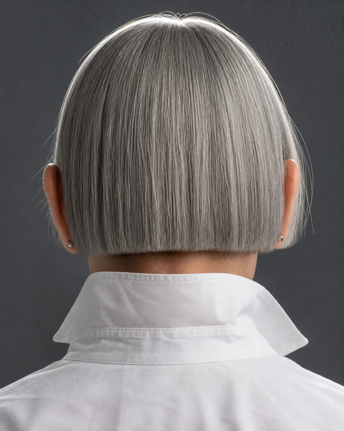 Back view close crop of a woman in her late 50s showing a perfectly geometric one-length silver bob with clean blunt nape line, white shirt against a charcoal wall
