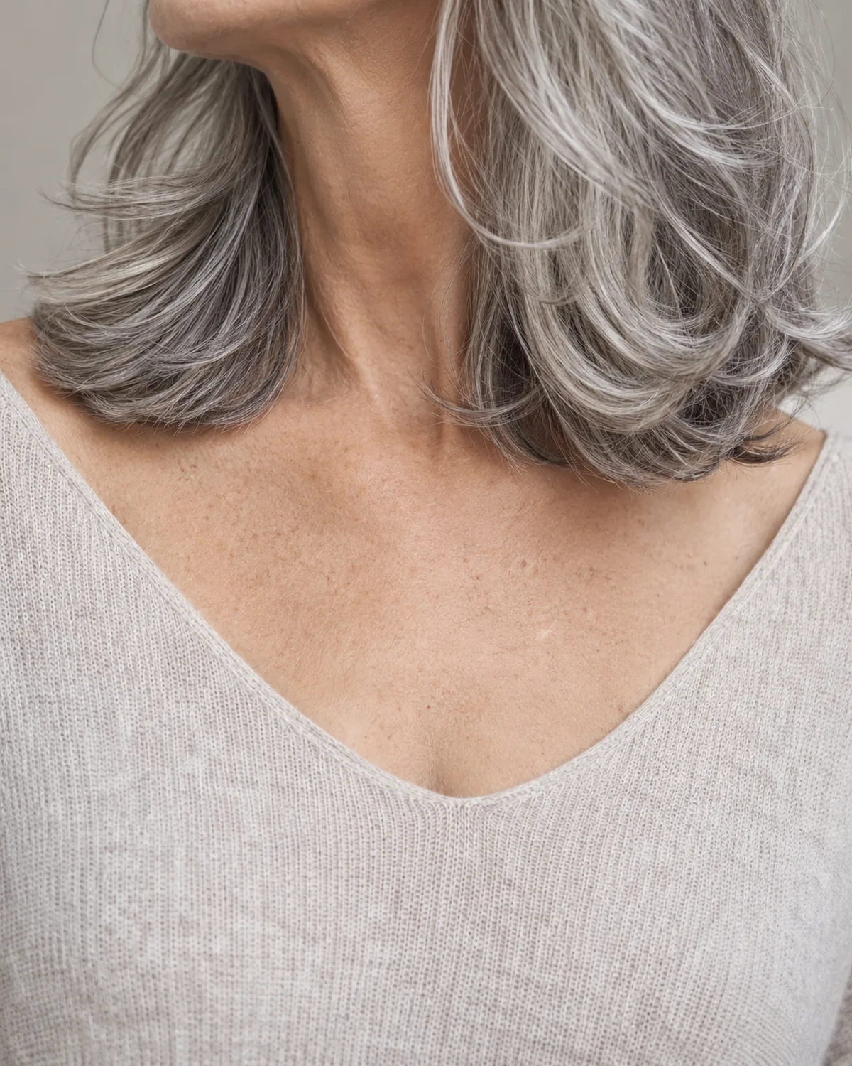 Close-up of layered silver-gray hair at collarbone level, showing weighted ends with wavy texture