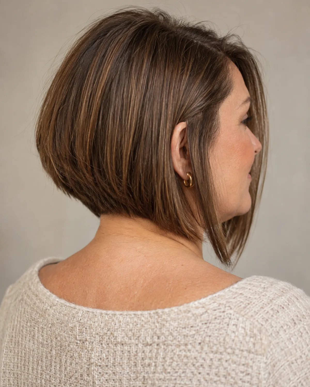Back-three-quarter view of a mature woman with an A-line bob, shorter at the nape and longer toward the front, warm brown hair showing the graduated nape line