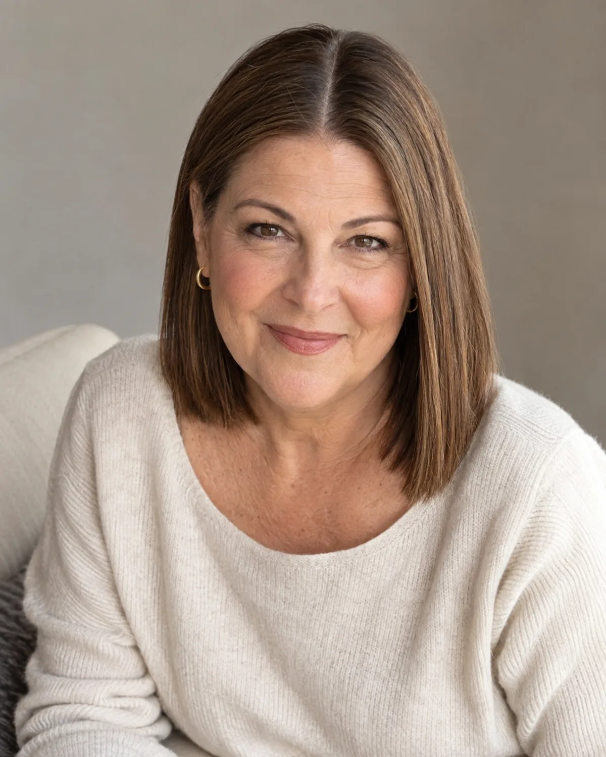 Mature woman seated with a blunt below-chin lob parted near the centre, straight warm chestnut hair with even ends