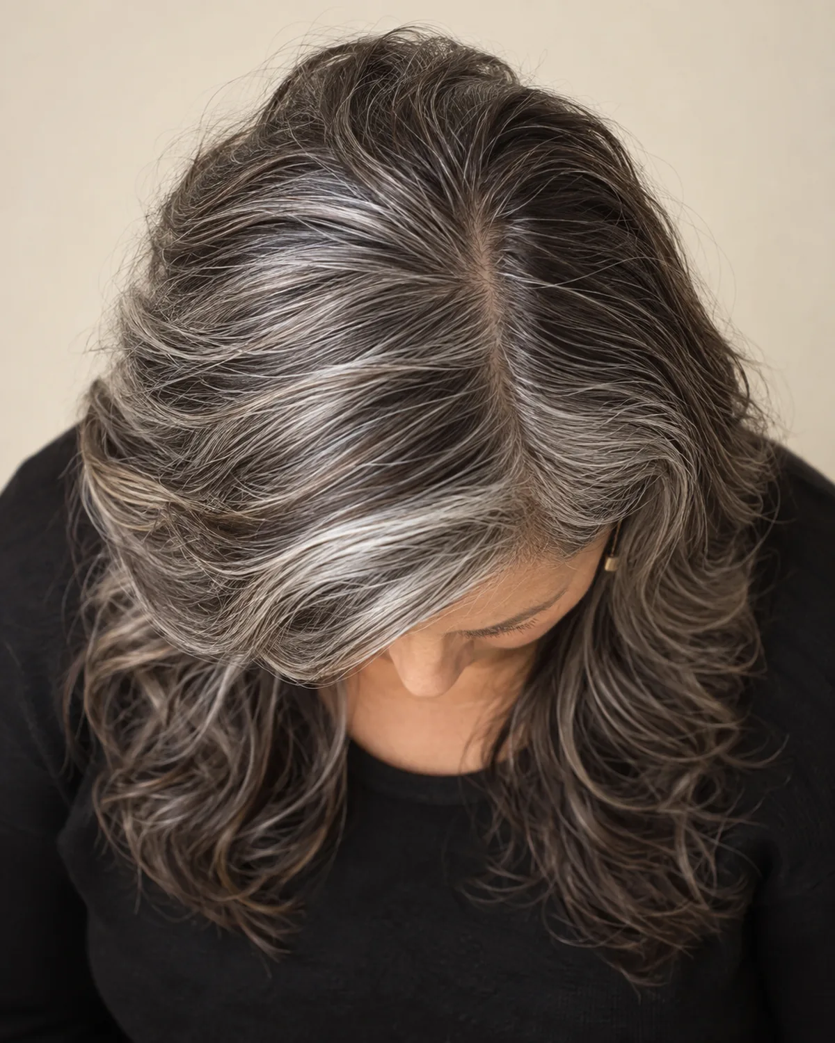 Top-down view of a mature woman with long salt-and-pepper hair, the crown showing visible volume and a side part, layers cascading from the crown downward