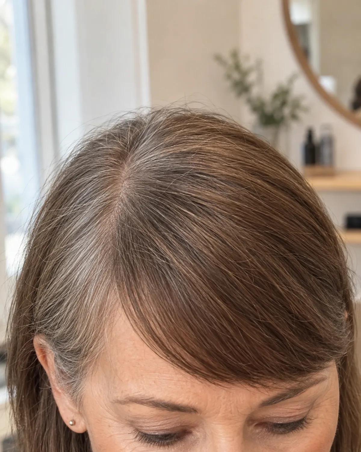 Close crop on the forehead and brow of a mature woman showing dense blunt side-swept bangs sweeping from a deep side part, fine hair