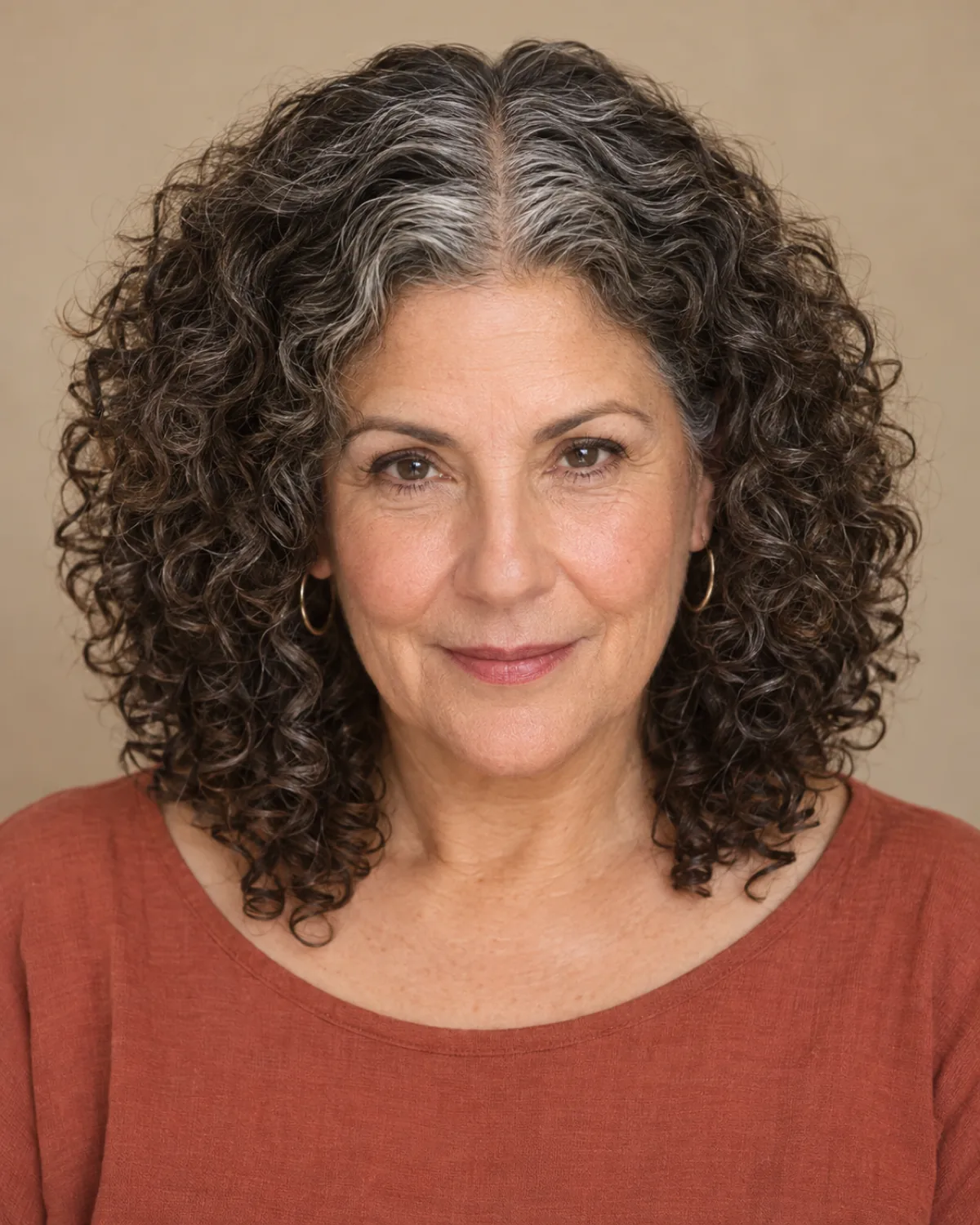 Front-facing mature woman with medium-length curly hair and precisely defined center part, curls falling symmetrically