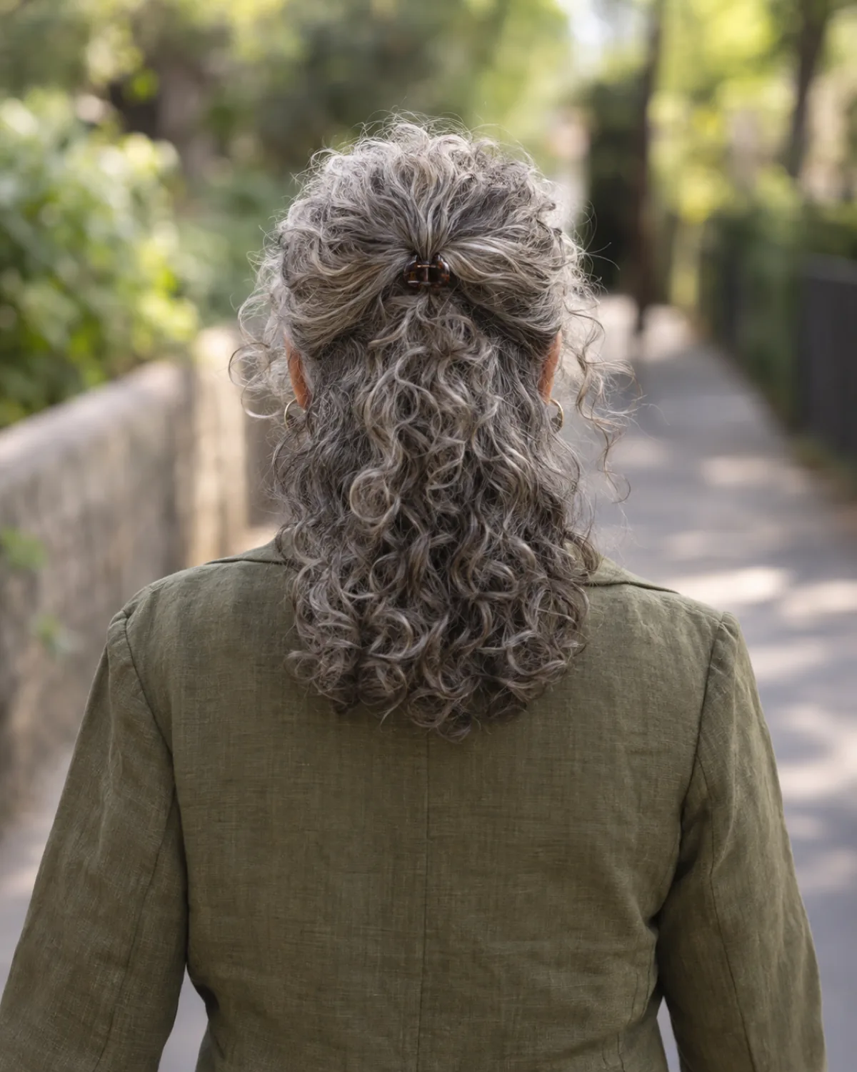 Mature woman walking away, natural curly hair pulled half-up at the crown with loose curls below the shoulder