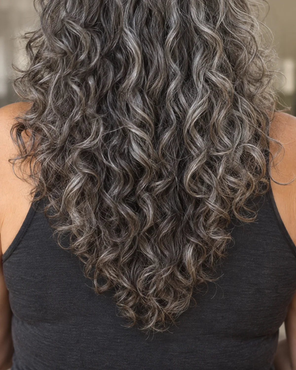 Close crop on long curly hair from mid-shoulder to tips showing V-cut perimeter creating rounded cascade
