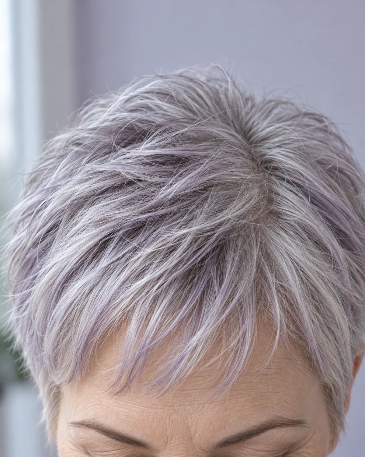 Close crop on fringe and brow line of mature woman with silver-lavender tinted short hair, subtle cool lavender cast