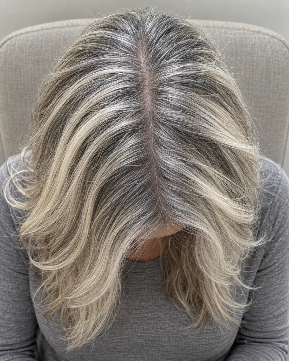 Top-down view of mature woman's crown showing platinum highlights interwoven with natural gray base, stone-gray top