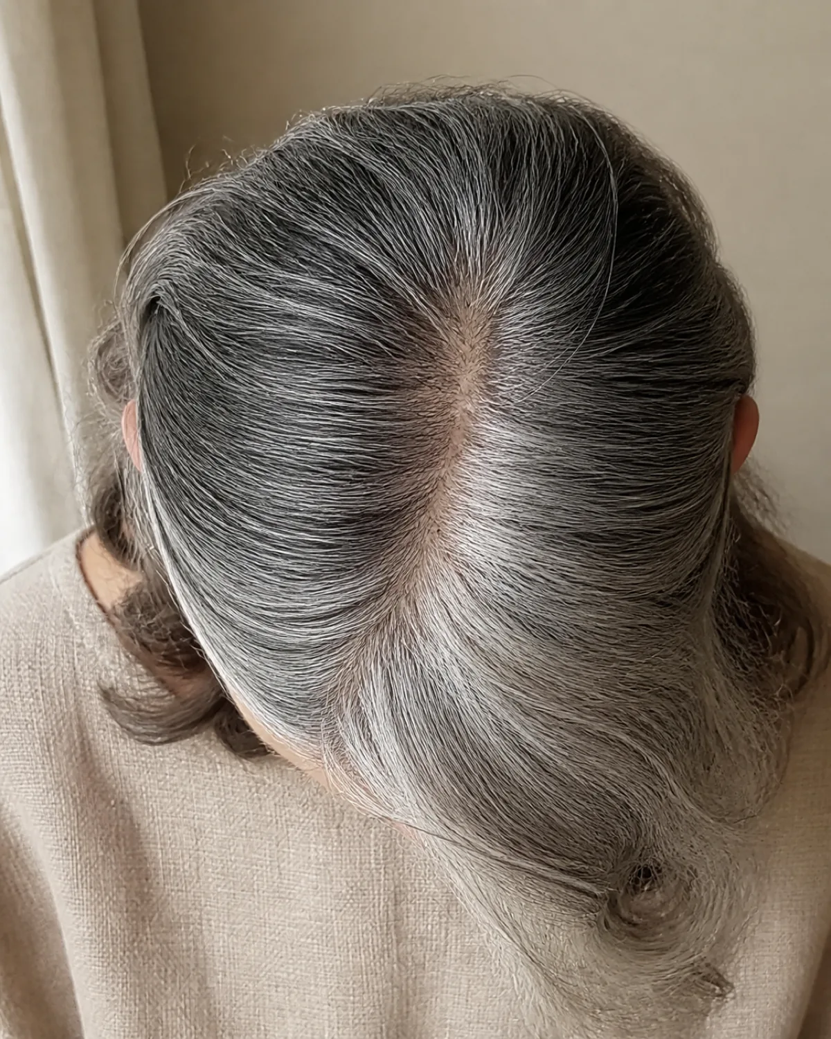 Top-down macro view of a mature woman's salt-and-pepper hair showing a deep side part with visible volume asymmetry between the two sides