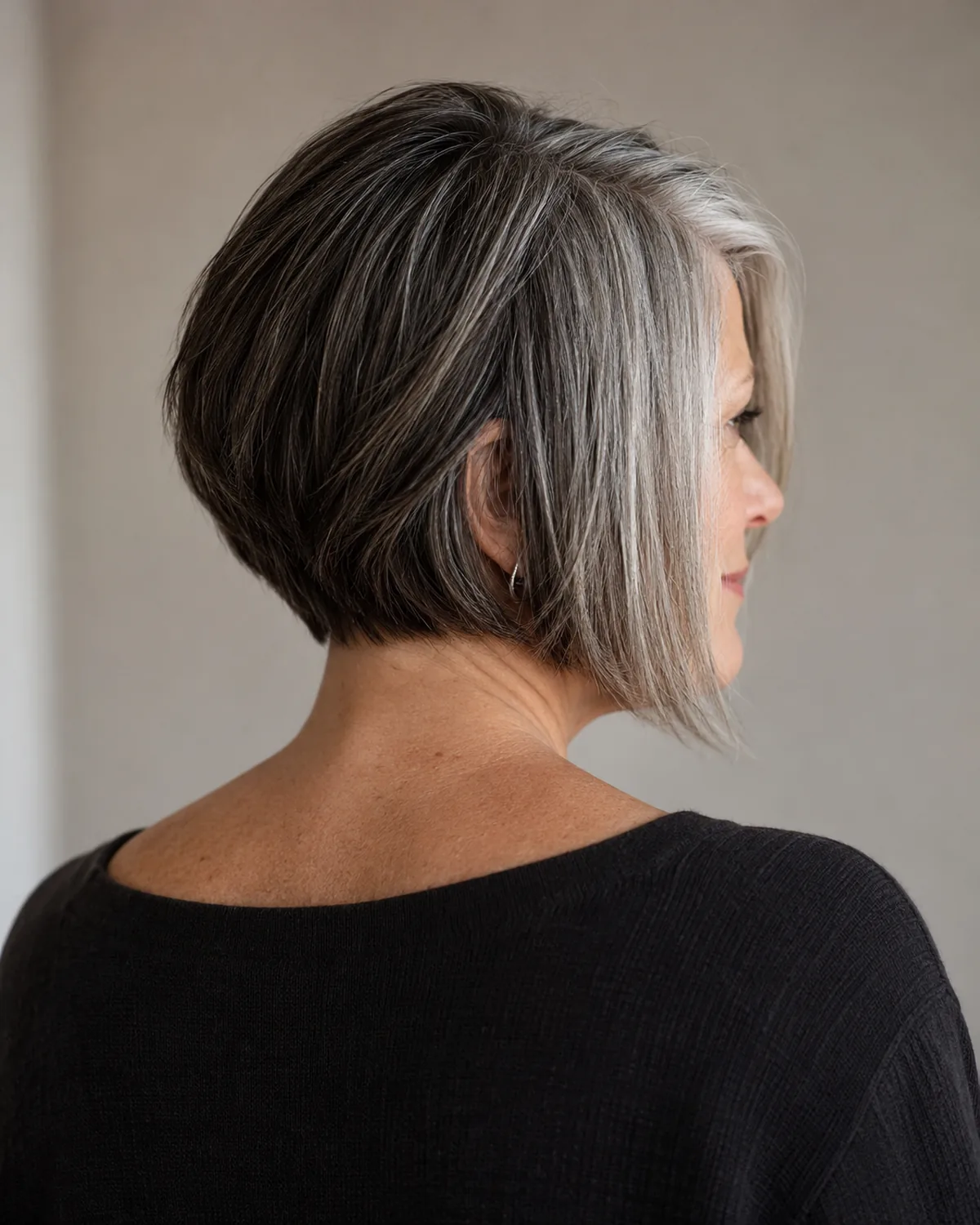 Back three-quarter right view of mature woman with asymmetric bob, longer silver-heavy side visible and shorter dark side tucked behind