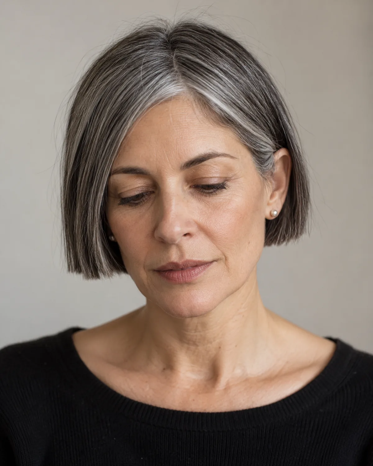 Front-facing mature woman with eyes downcast, blunt ear-length micro bob showing salt-and-pepper mix in a tight graphic frame