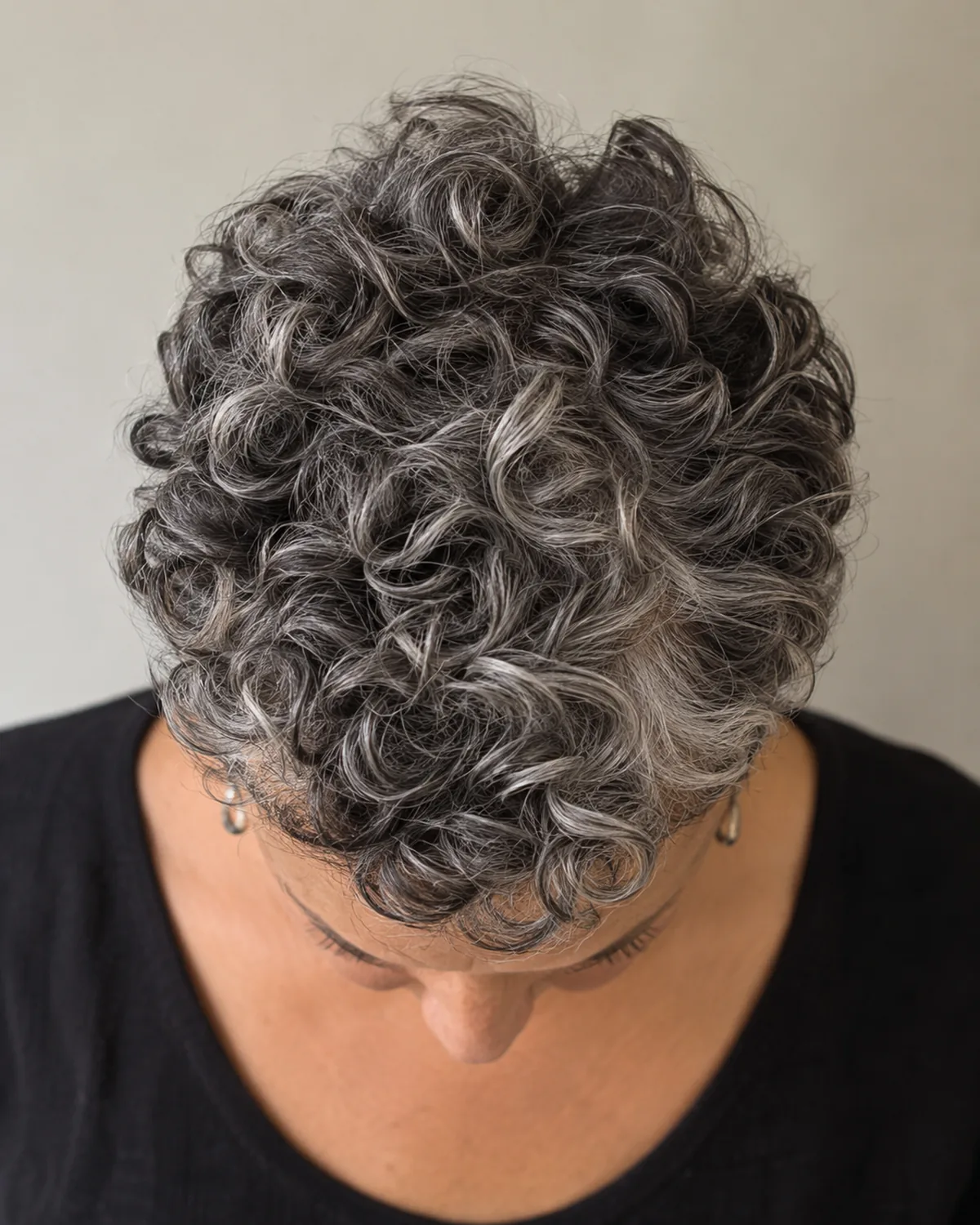 Top-down macro of mature woman with curly salt-and-pepper pixie, tight ringlets interleaving dark and silver strands