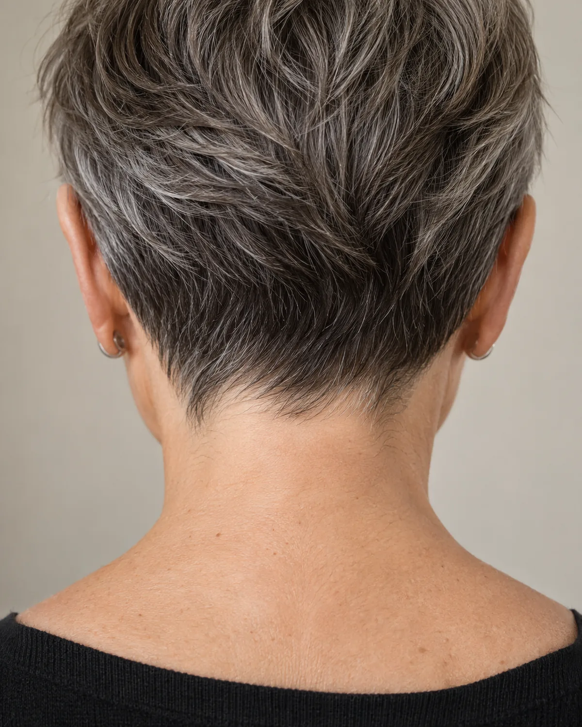 Back view of mature woman with natural-part pixie, salt-and-pepper growth line visible from nape to crown