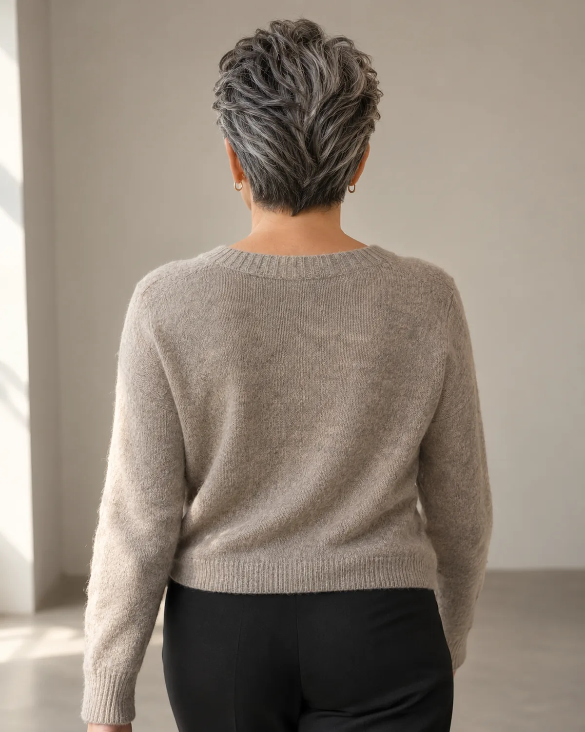 Back full standing view of mature woman with swept-back salt-and-pepper crop, curly texture showing the full color map from hairline to crown