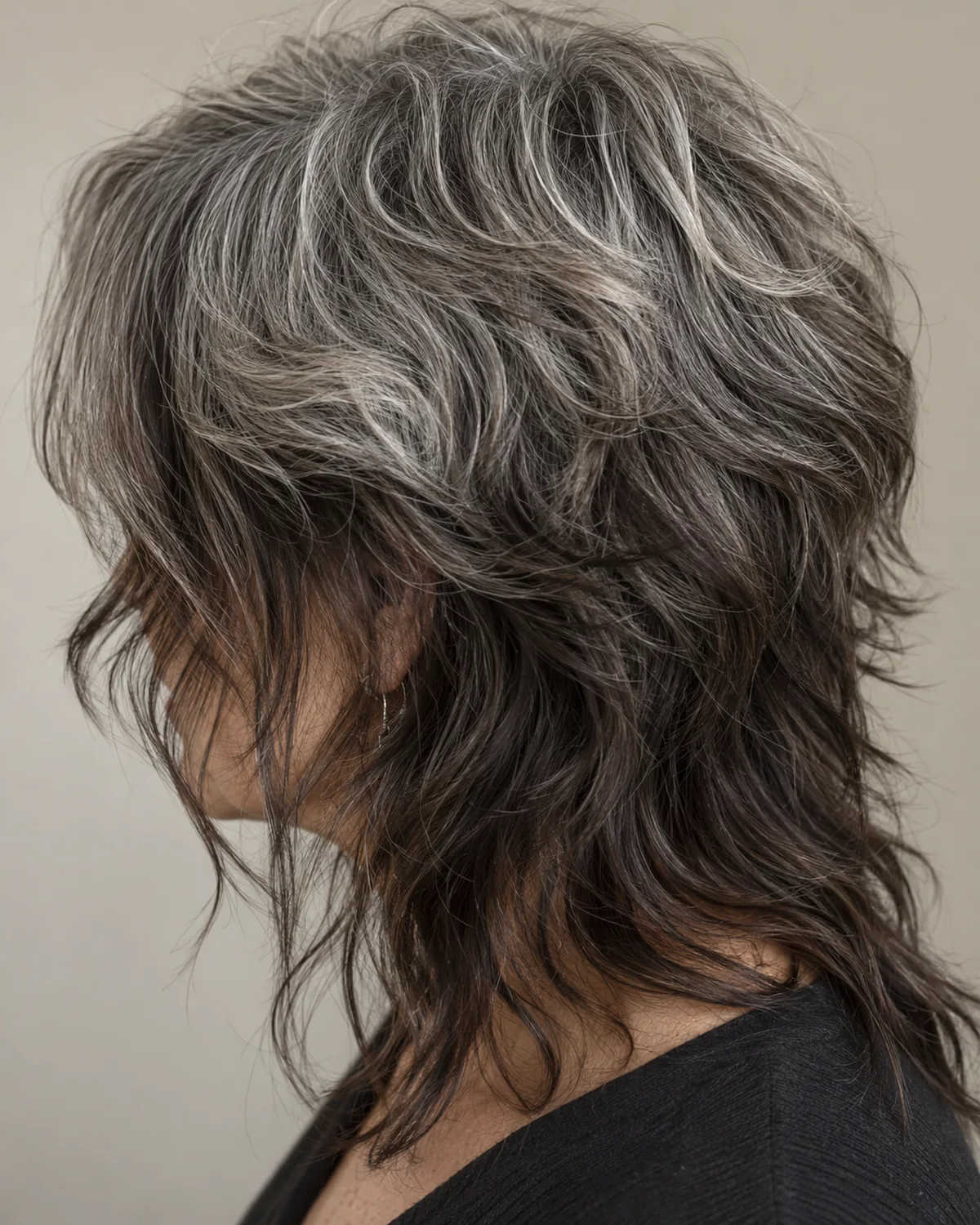Three-quarter right view of mature woman looking down with textured wolf cut, silver-threaded crown and darker longer lengths falling past the shoulders