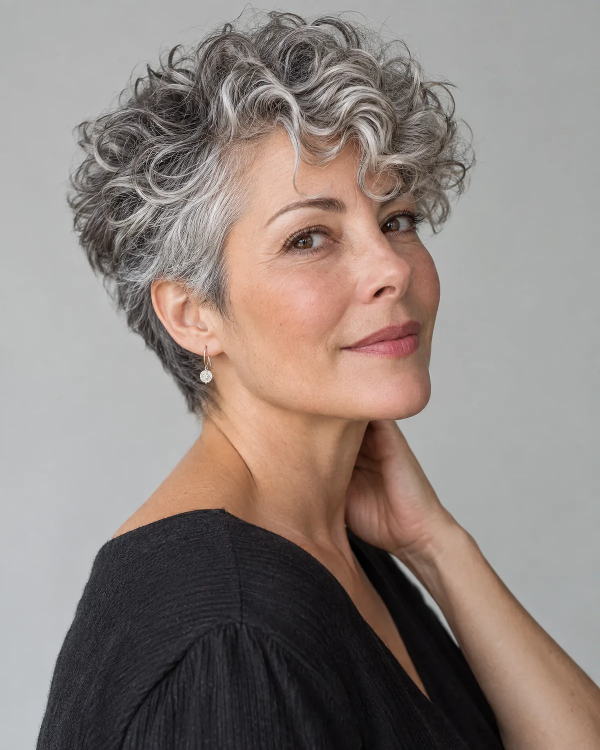 Three-quarter view of mature woman with elongated curly gray pixie, sharp nape taper and crown volume