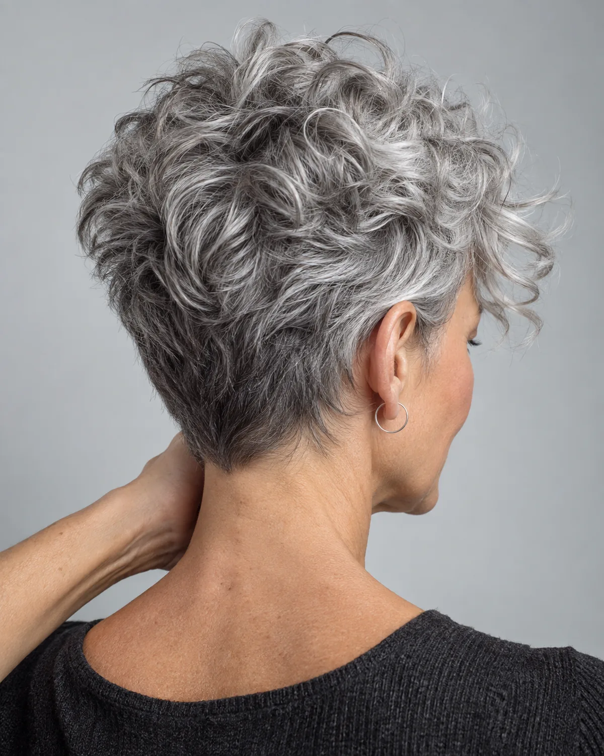 Back-three-quarter view of mature woman with silver pixie, crown curls 3-4 inches over close-cut back