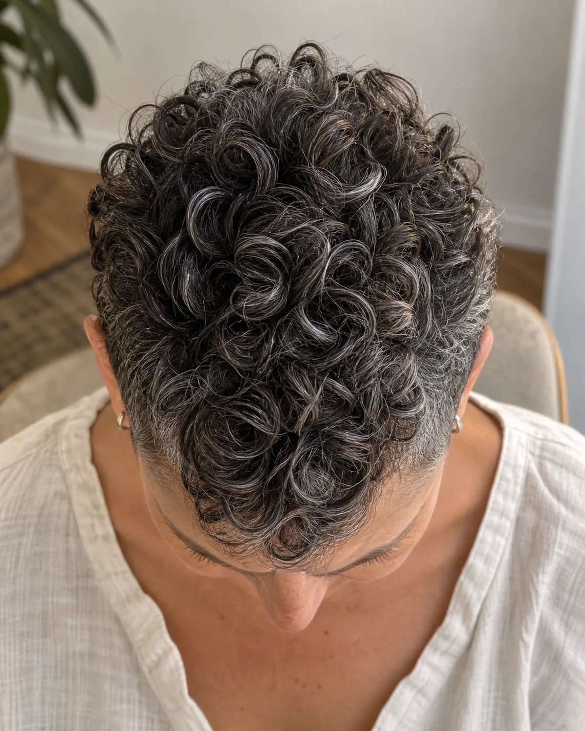 Top-down view of mature woman with tight salt-and-pepper curls in a pixie cut, crown curls standing with vertical lift, cropped sides