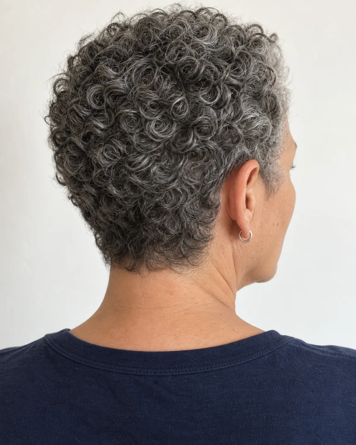 Close view of nape and hairline of mature woman with salt-and-pepper very short curly crop, tight uniform curl pattern, no product