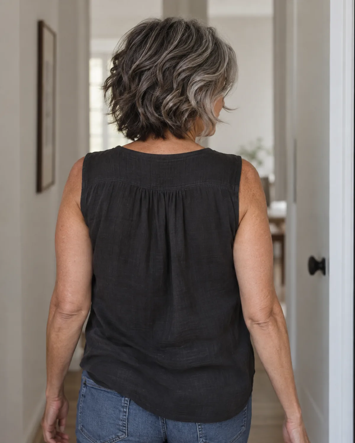 Rear view of a mature woman with thick salt-and-pepper wavy hair walking away in a cropped shag with heavy layers and curtain bangs visible at the sides