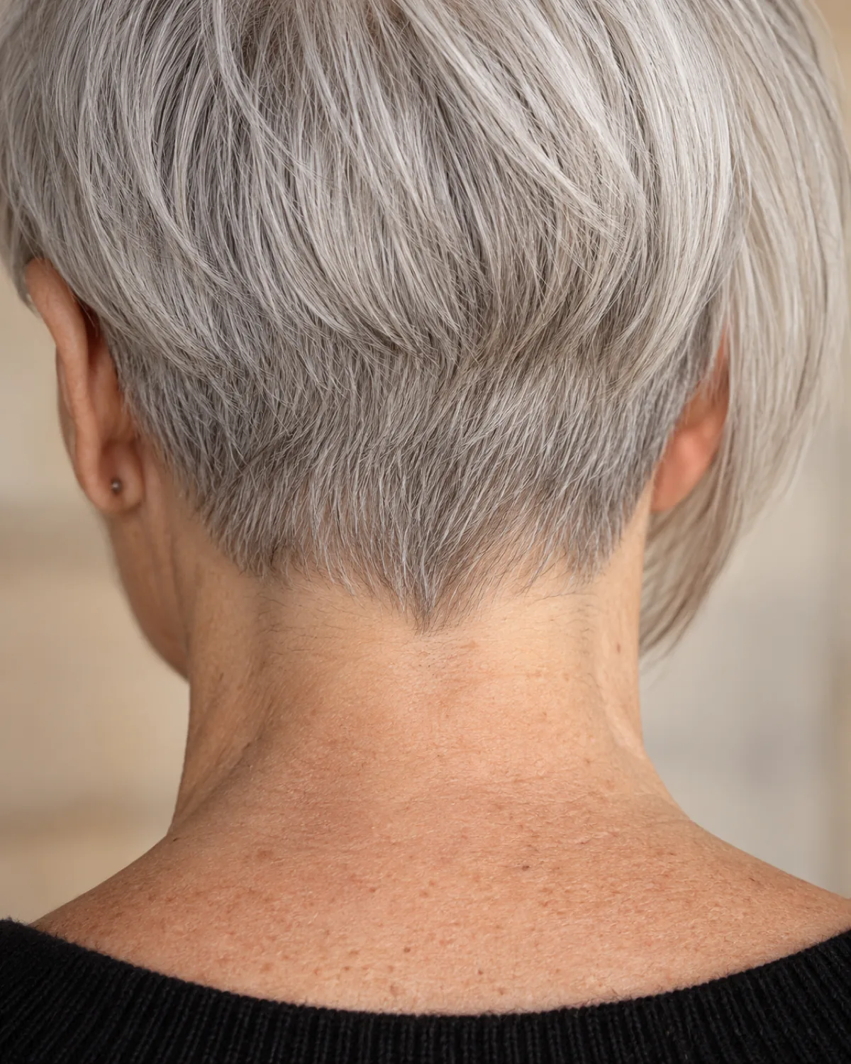 Close-up of the nape and back hairline of a mature woman over 60 with a cropped back, very short silver hair at the nape showing clean hairline and forward-falling fringe transition