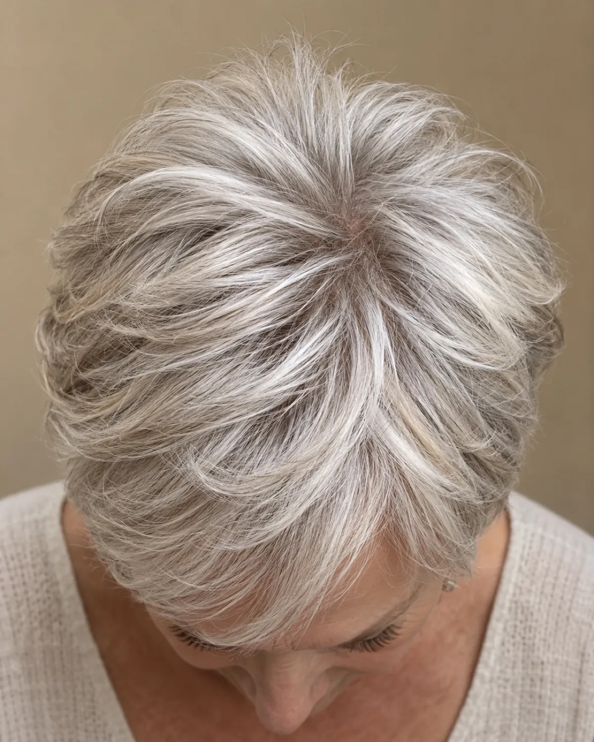 Overhead view of the crown of a mature woman over 60 with feathered pixie, showing lifted feathered layers creating height and volume at the top in silver hair