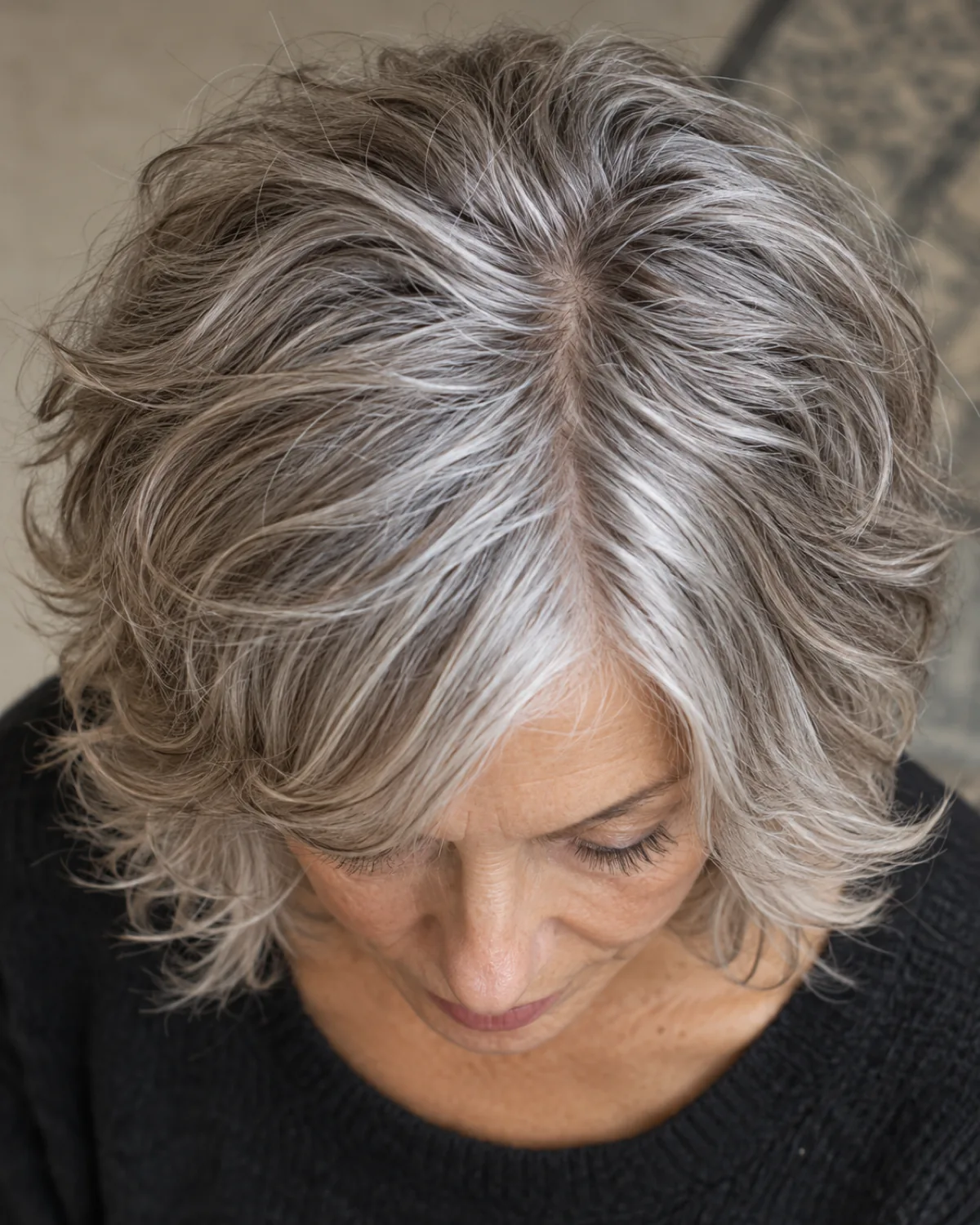 Overhead view of the crown and layered movement of a mature woman over 60 with a layered shag in wavy grey hair, shorter crown layers and curtain fringe visible