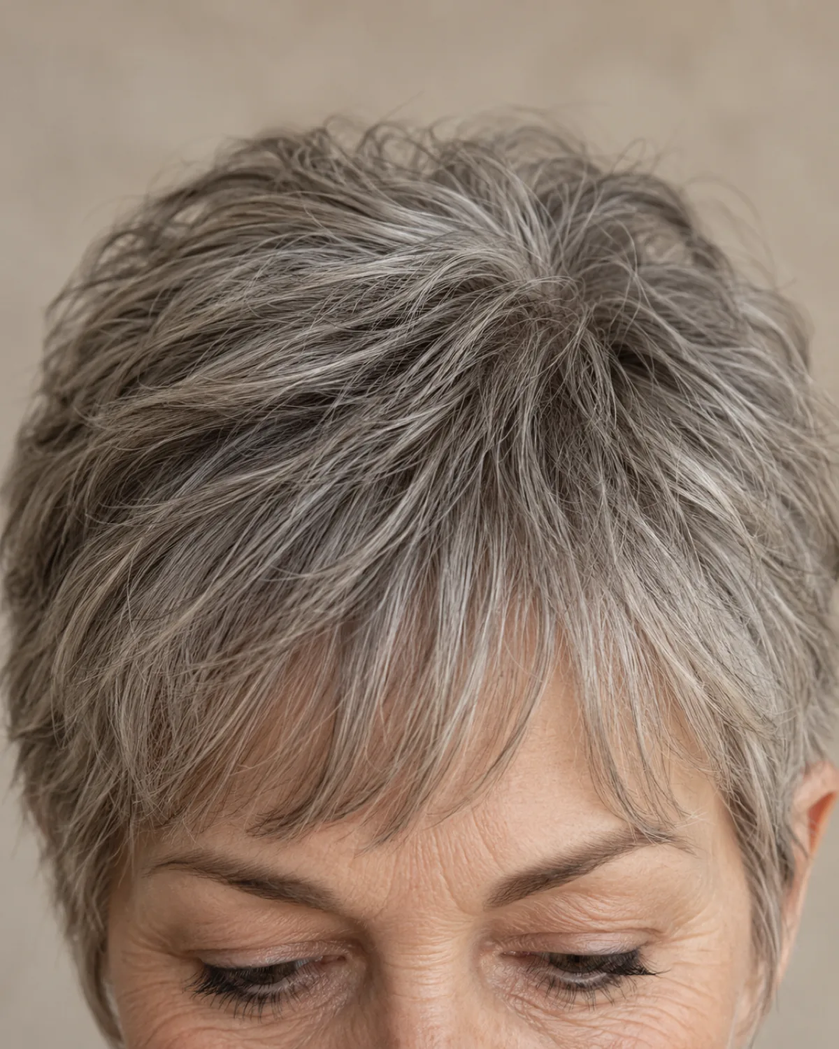 Close-up of the crown and fringe area of a mature woman over 60 with a textured crop, point-cut texture visible in grey hair with soft bangs at the brows