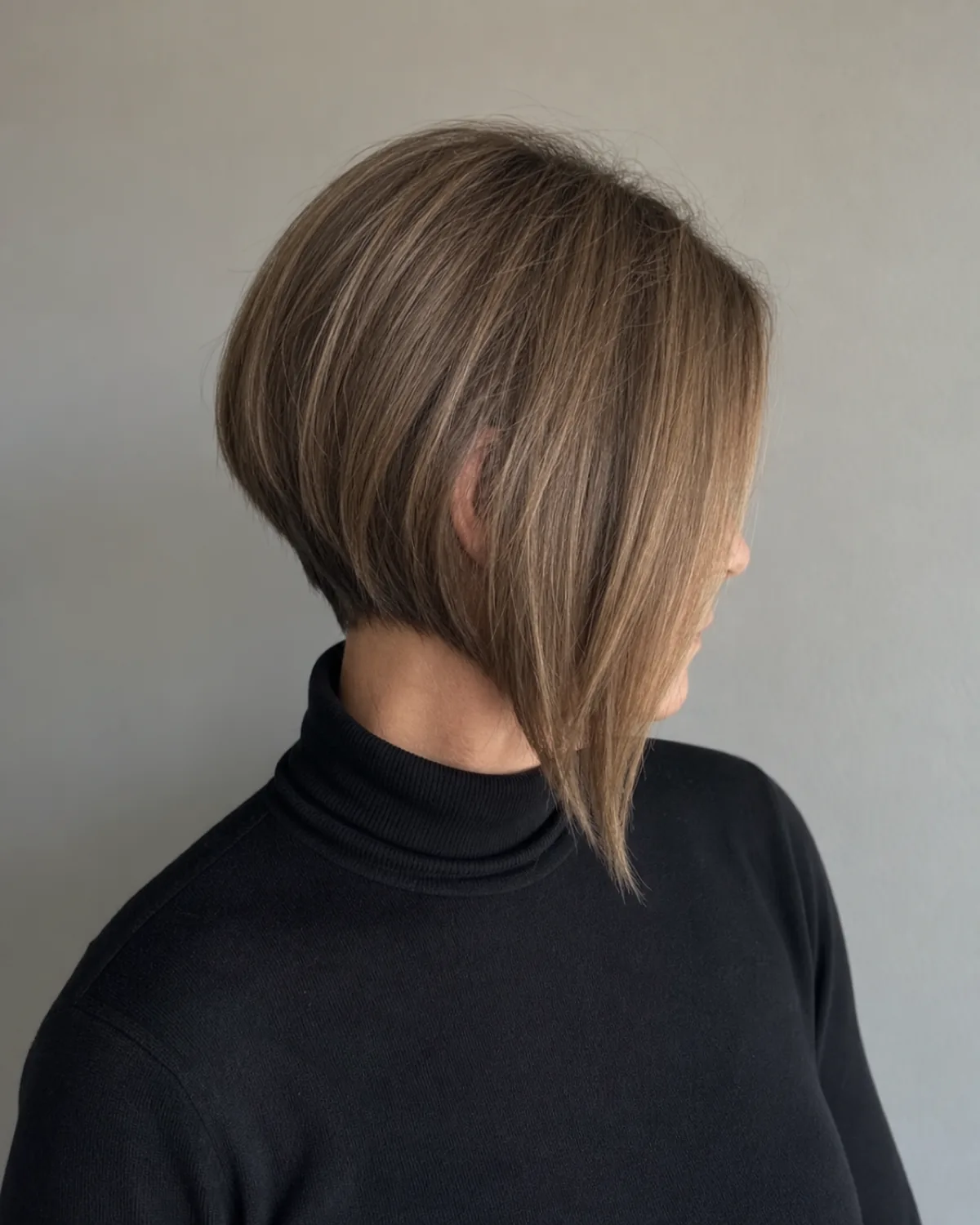 A woman turned three-quarters to the camera in a black roll neck, her ash brown bob visibly shorter at the nape and falling past the jaw toward the collarbone at the front