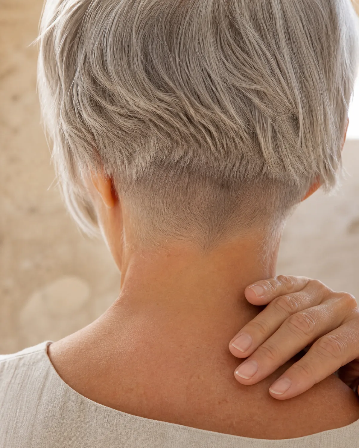 Close-up of a woman's nape and the back of her head showing cool silver hair with a cropped nape and ear-length top, the contrast between the very short nape and the longer top hair clearly visible