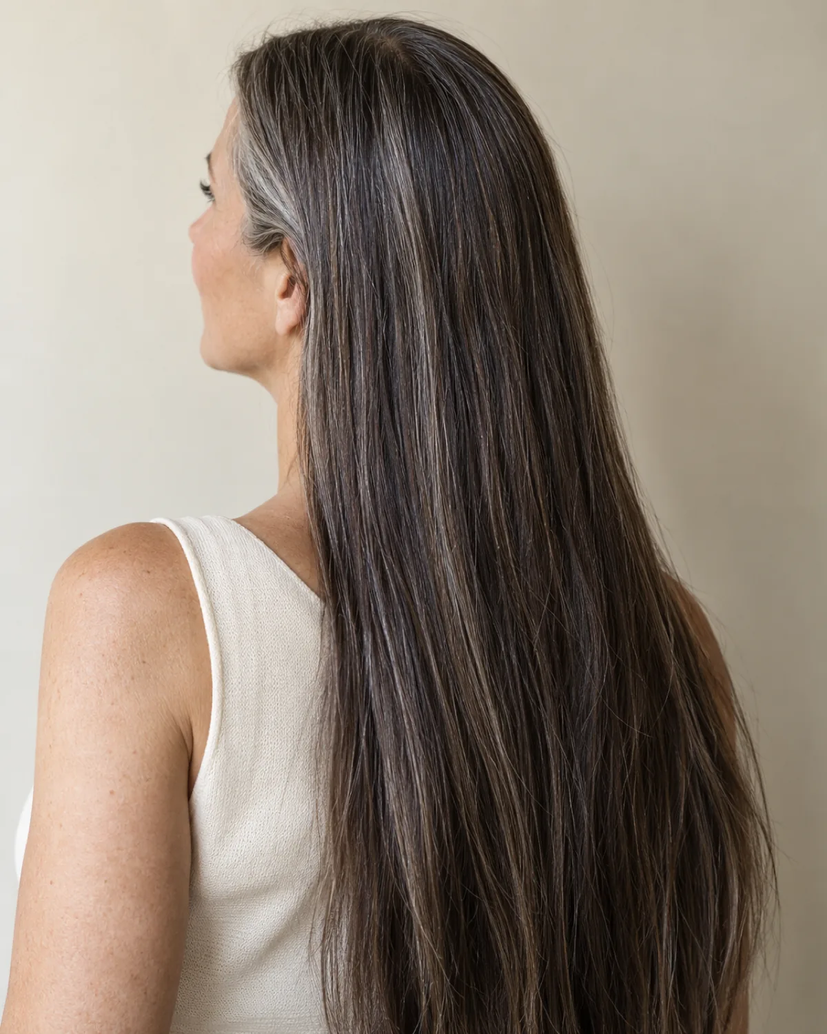 Back three-quarter view of mature woman with very long sleek dark straight hair with silver threading, middle part visible