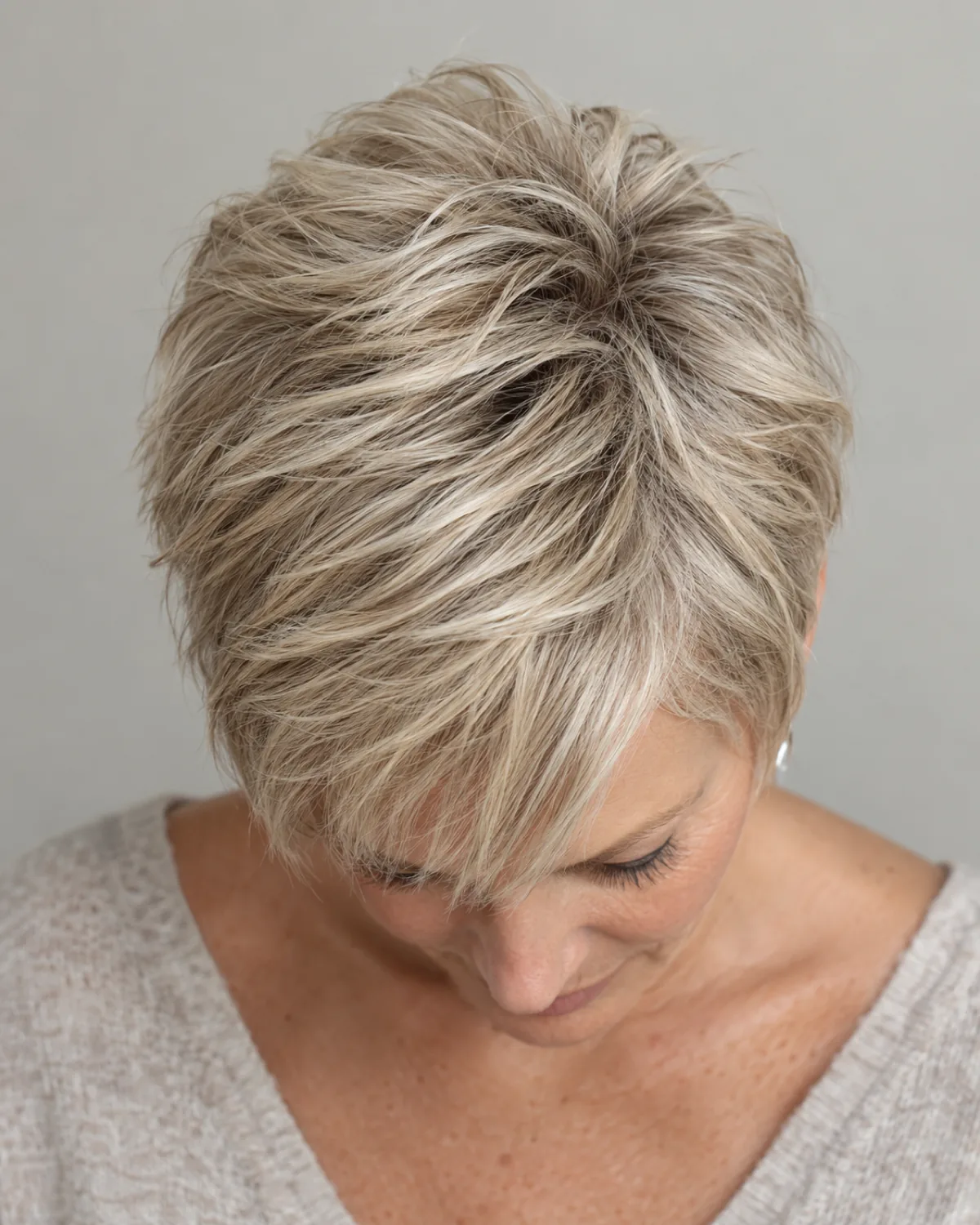 Top-down view of mature woman with short textured pixie cut in ash blonde, point-cut texture visible through the crown
