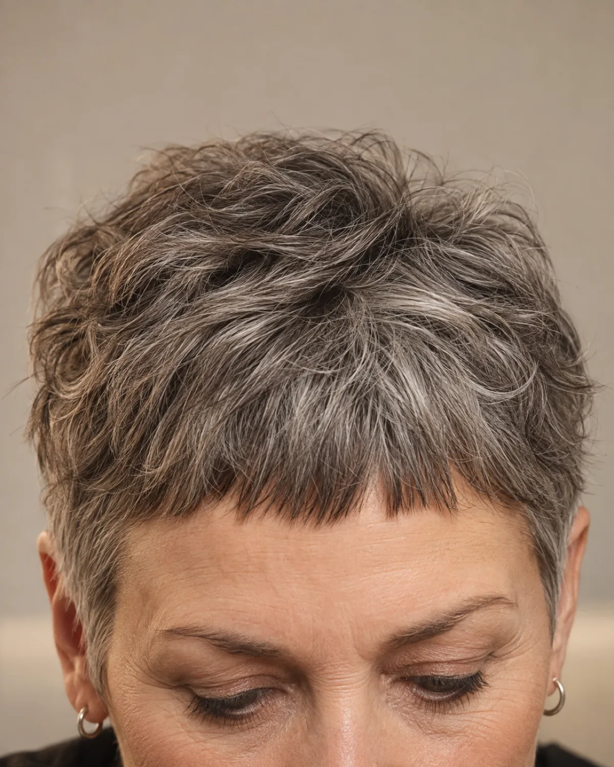 Close crop on the fringe and brow line of woman over 50 with steel grey wavy textured crop, micro fringe cut above the eyebrows, warm light